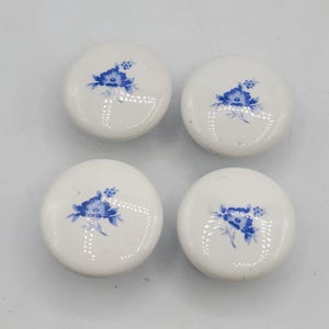 Peut inclure: Quatre boutons de placard en céramique blanche avec un motif floral bleu. Chaque bouton a une forme arrondie et une finition brillante. Le motif floral bleu est centré sur chaque bouton, ajoutant une touche d'élégance.