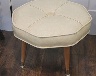 Vintage Mid-Century Modern footstool featuring a cream vinyl tufted octagonal top with tapered wooden legs and brass-tipped