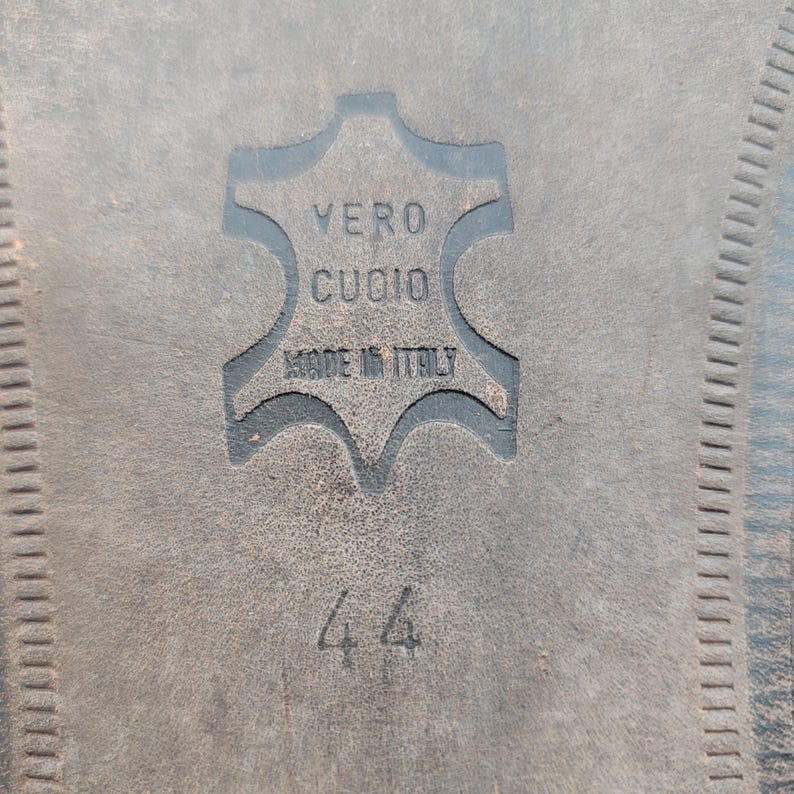 May include: Close-up of a shoe sole with the embossed text "VERO CUOIO MADE IN ITALY". The number "44" is also visible. The sole is dark gray and has a textured surface.