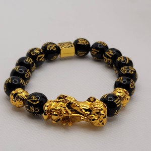 May include: Black beaded bracelet with gold accents and a gold dragon charm. The beads are inscribed with Chinese characters.