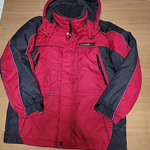 Puede incluir: Chaqueta de invierno con capucha roja y negra. La chaqueta tiene capucha y mangas negras, con un cuerpo rojo. Cuenta con cierre de cremallera, múltiples bolsillos y un pequeño logotipo en el pecho. La chaqueta está diseñada para el frío.