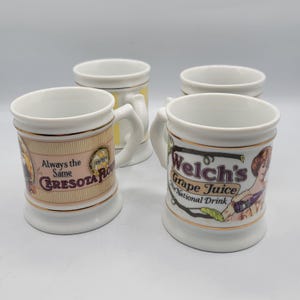 Puede incluir: Cuatro tazas de cerámica blanca con ribetes y asas doradas. Dos tazas presentan anuncios vintage de Cersota Flour y Welch's Grape Juice. Las tazas tienen una estética clásica y vintage.