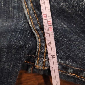 Puede incluir: Primer plano de una cinta m&eacute;trica blanca con marcas negras, que mide 86,36 cent&iacute;metros. La cinta est&aacute; colocada sobre un par de pantalones vaqueros azules.