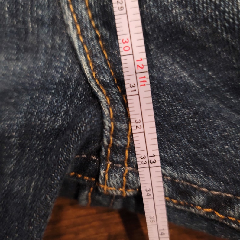 Puede incluir: Primer plano de una cinta m&eacute;trica blanca con marcas negras, que mide 86,36 cent&iacute;metros. La cinta est&aacute; colocada sobre un par de pantalones vaqueros azules.