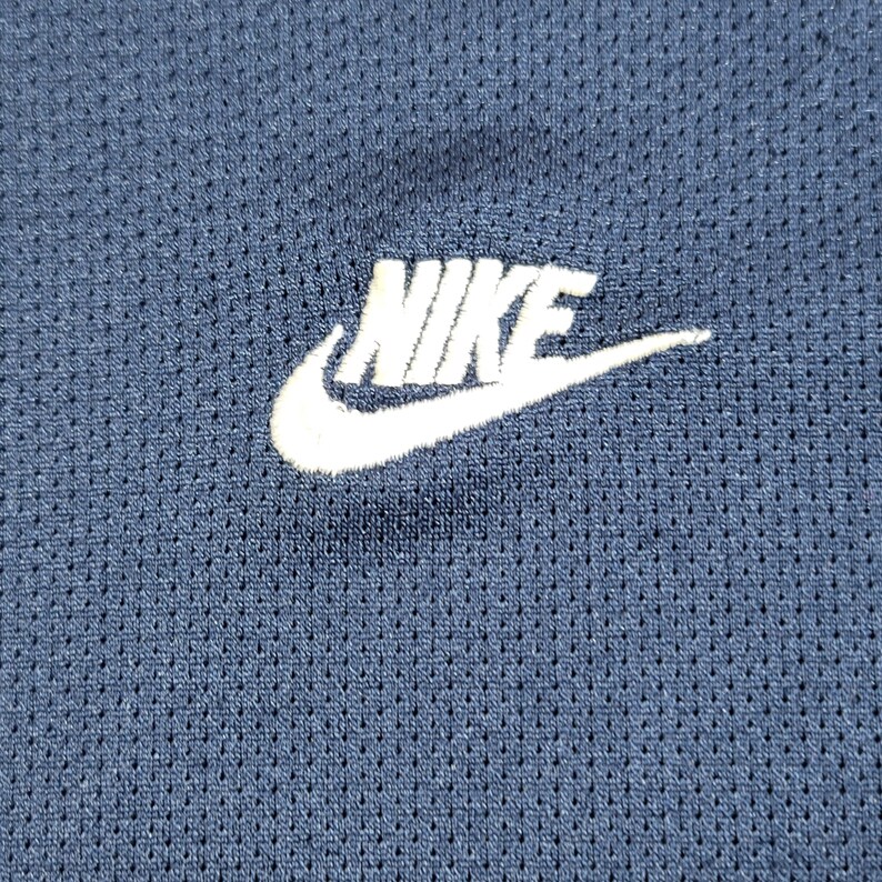Puede incluir: Un logotipo blanco de Nike sobre una tela azul marino con un patr&oacute;n texturizado.