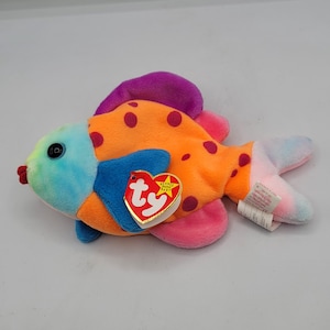 May include: A colorful plush fish toy with orange body, purple spots, and a blue and purple fin. The fish has a blue eye and a red mouth. A heart-shaped tag is attached to the fish.