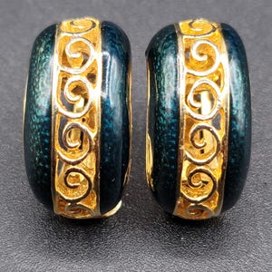 May include: A pair of gold-coloured hoop earrings with a dark teal enamel finish. The earrings have a gold filigree design on the front and sides. A classic, elegant accessory.