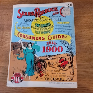 Pode incluir: Uma capa de catálogo vintage "Consumers Guide" da Sears, Roebuck and Co. do outono de 1900. A capa apresenta uma mulher em um vestido turquesa, uma cornucópia e ilustrações de edifícios. O título do catálogo está em letras grandes e coloridas.