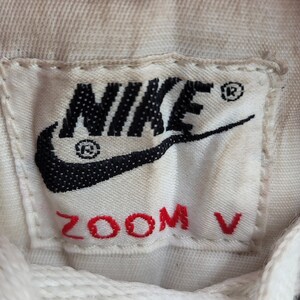 May include: White athletic shoe with a black Nike swoosh logo and red "ZOOM V" text on the tongue.