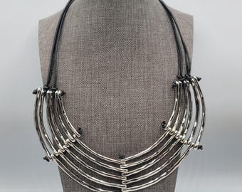 Collar llamativo con tubos de plata y cordón de cuero negro multifilamento anudado.