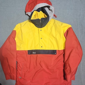 Könnte beinhalten: Vintage Anorak-Jacke in Rot, Gelb und Grau. Die Jacke hat eine Kapuze, einen Reißverschlusskragen und eine Vordertasche mit dem Text "For Wild". Die Jacke hat einen Knopfverschluss und elastische Bündchen.