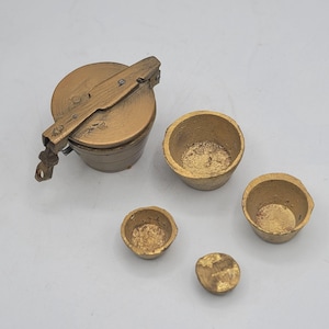 May include: A set of gold-coloured metal objects including one lidded container with a hinged latch mechanism and three open, bowl-shaped vessels of varying sizes. The surfaces have a textured, metallic finish with visible signs of wear.
