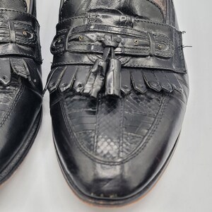 May include: Close-up of a pair of black leather loafers. The shoes feature a textured vamp, decorative tassels, and fringe detailing. The leather appears to be in good condition, with a polished finish. The shoes have a classic, timeless design.