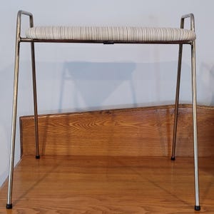May include: A vintage vanity stool with a striped seat cushion and chrome legs. The seat is approximately 24 inches long and 12 inches wide. The legs are slender and angled, with black rubber feet.