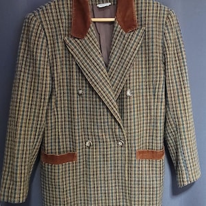 May include: A double-breasted blazer with a plaid pattern in shades of brown, green, and blue. The blazer has a brown velvet collar and pocket accents, with silver-coloured buttons. The jacket is hanging on a wooden hanger.