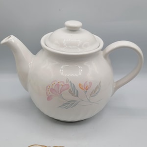 Könnte beinhalten: Weiße Teekanne aus Keramik mit einem Blumendesign mit rosa und orangefarbenen Blumen. Die Teekanne hat einen Deckel und einen Griff.