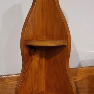 Op de afbeelding: Een houten hoekplank met twee planken. De plank is gemaakt van natuurlijk hout met een bruine vlek. De plank is gevormd als een fles.
