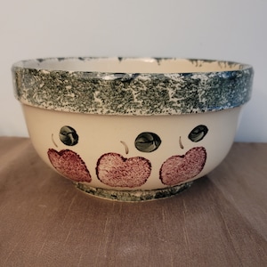 Puede incluir: Un tazón mezclador de cerámica grande de color crema con un borde verde y tres manzanas rojas pintadas en el lateral.