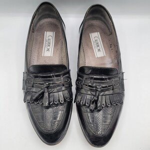 May include: Pair of black leather loafers with a textured vamp and decorative fringe. The shoes have a classic design with a pointed toe and a small heel. The brand name "CALDERONE" is visible inside the shoe.