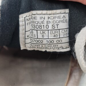 May include: A black and white shoe size tag with the text "MADE IN KOREA FABRIQU&Eacute; EN COR&Eacute;E 930810 ST US UK EUR CM M7/W8.5 6 40 25 107002 100 00 PATENT #4,562,651 AND FOREIGN PATENTS".