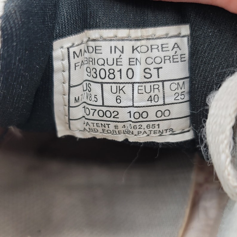 May include: A black and white shoe size tag with the text "MADE IN KOREA FABRIQU&Eacute; EN COR&Eacute;E 930810 ST US UK EUR CM M7/W8.5 6 40 25 107002 100 00 PATENT #4,562,651 AND FOREIGN PATENTS".