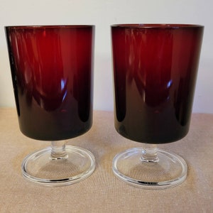 May include: Two clear glass goblets with a red ombre design. The goblets have a short stem and a wide base.