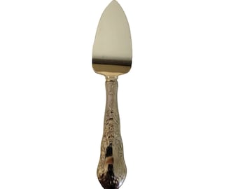 May include: A silver cheese knife with an ornate handle. The blade is pointed and the handle is decorated with a floral design.
