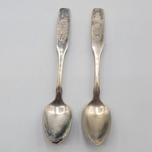Peut inclure: Deux cuillères en argent avec un motif de visage d'homme sur le manche. Les cuillères sont sur un fond blanc.