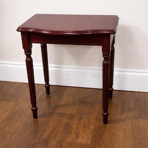 May include: A small, dark cherry-coloured side table with a curved top and four turned legs. The table is made of wood and has a glossy finish. The table is a classic design, suitable for a living room or bedroom.