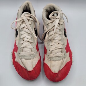 May include: A pair of white and red running shoes with black accents. The shoes have a white canvas upper with red trim around the toe and heel. The laces are white and the shoes have a black rubber sole.