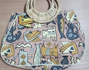 May include: A woven straw tote bag with a pink and yellow patterned fabric. The pattern features stylized animals and geometric designs. The bag has a woven straw handle.
