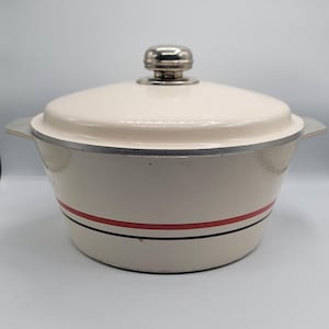 May include: Cream-coloured cast iron Dutch oven with a matching lid and silver-toned handle. The pot features a red and black stripe around the middle. The lid has a silver-toned knob.