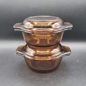 Puede incluir: Dos fuentes de vidrio color ámbar con tapas apiladas. Cada fuente tiene forma cuadrada con bordes redondeados y dos asas. Las tapas son transparentes y encajan perfectamente. Las fuentes están hechas de un material de vidrio duradero.