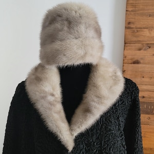 Könnte beinhalten: Ein schwarzer Vintage-Mantel mit einem hellfarbigen Pelzkragen und passendem Pelzhut. Der Mantel hat ein strukturiertes Aussehen, und das Fell ist hellgrau. Der Hut ist ein klassischer Stil.