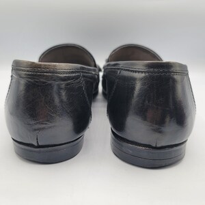 May include: Pair of black leather loafers. The shoes have a glossy finish and a classic design. The image shows the back of the shoes, highlighting the heel and sole details. The loafers appear to be well-worn.