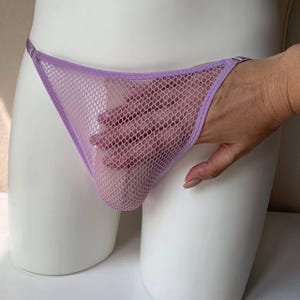 Könnte beinhalten: Ein lavendelfarbener Mesh-String. Die Unterwäsche besteht aus einem feinen, offen gewebten Material. Der String hat einen dünnen Bund und eine dreieckige Vorderseite. Die Unterwäsche wird auf einer weißen Schaufensterpuppe präsentiert.