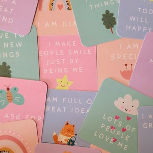 May include: A set of colorful affirmation cards with illustrations and positive messages. The cards feature phrases like "I am kind", "I make people smile just by being me", and "Lots of people love me".