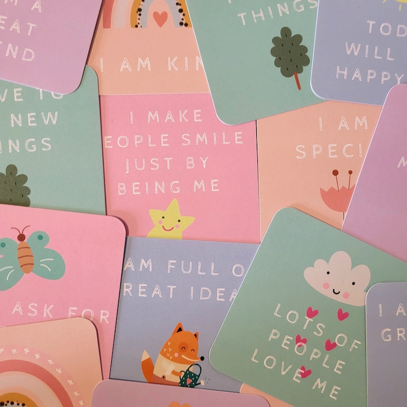 May include: A set of colorful affirmation cards with illustrations and positive messages. The cards feature phrases like "I am kind", "I make people smile just by being me", and "Lots of people love me".
