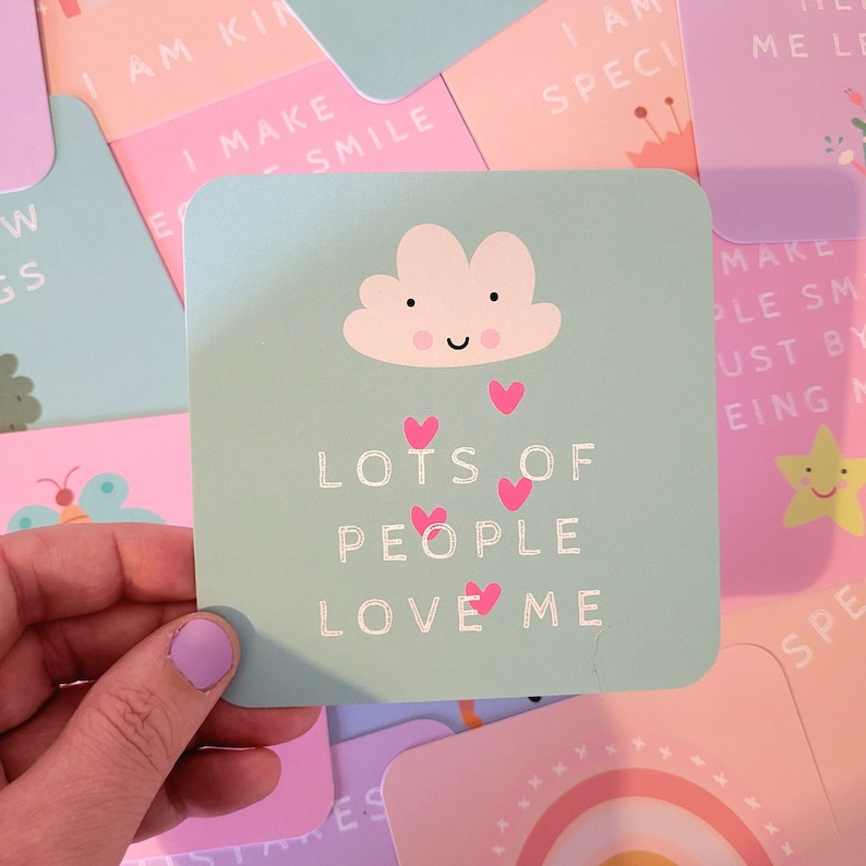 May include: A light blue card with a white cloud and pink hearts. The text on the card reads "Lots of people love me".