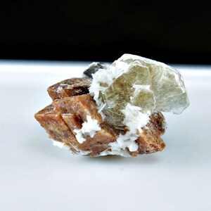 May include: A cluster of brown and white crystals with a larger, translucent, light brown crystal on top.