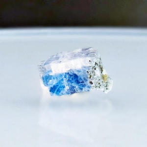 May include: A small, blue and white crystal with a rough, irregular shape. The crystal has a translucent appearance and is likely a natural mineral.