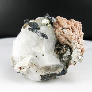 May include: A cluster of white, clear, and pink crystals with black and green accents. The crystals are arranged in a natural, organic formation.