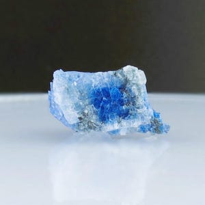 May include: A small, rough, blue and white crystal with a jagged edge.