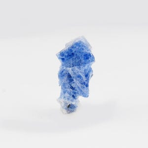 May include: A raw, crystalline mineral specimen featuring a vibrant blue colour with translucent and opaque sections. The structure is irregular and jagged, displaying natural facets and a rough, textured surface throughout the entire formation.