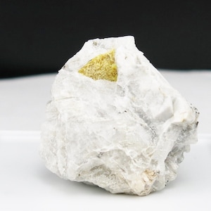 May include: A small, white, rough-textured rock with a yellow, triangular crystal embedded in it.