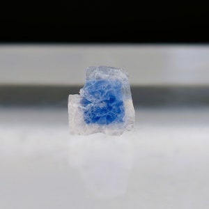 May include: A small, clear crystal with a blue center. The crystal has a rough, irregular shape.