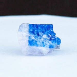May include: A raw, natural gemstone with a striking contrast of white and deep blue hues. The stone's surface has a rough, textured appearance, showcasing its organic form. This unique piece could be used for jewelry or display.