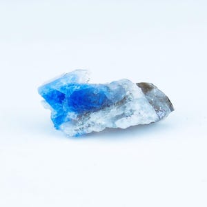 May include: A raw, natural crystal formation with striking blue and white coloration. The crystal's surface has a rough, textured appearance, with areas of deep, saturated blue contrasting against lighter, translucent sections. The overall shape is irregular and organic.