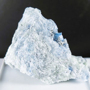 May include: A rough, light blue and white rock with a crystalline texture. The rock has a jagged, irregular shape.