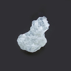 Peut inclure: Un spécimen de cristal blanc brut et translucide, présentant une forme irrégulière et dentelée ainsi qu'une texture de surface rugueuse et à facettes. Le minéral montre divers degrés de clarté et des fractures internes, reflétant la lumière.